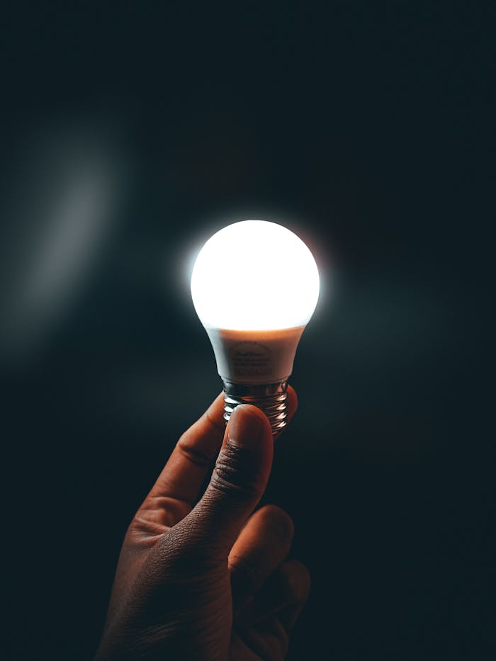 A close-up of a hand holding a bright LED light bulb against a dark background.