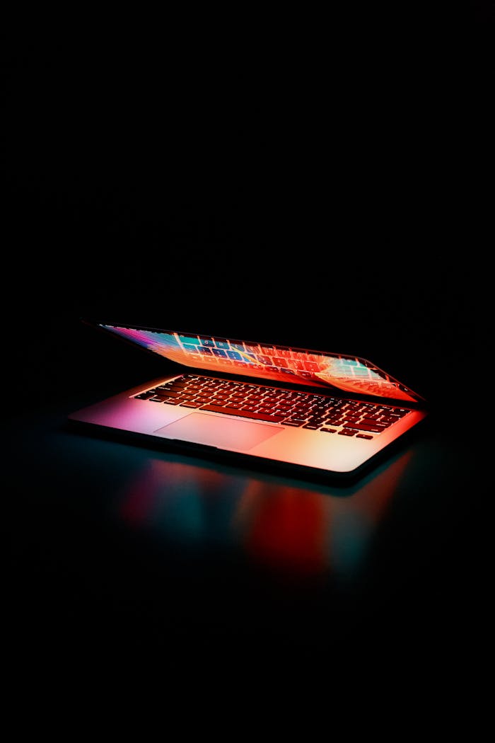 ours-journey Laptop partially opened, emitting vibrant multicolored lights in dark setting.