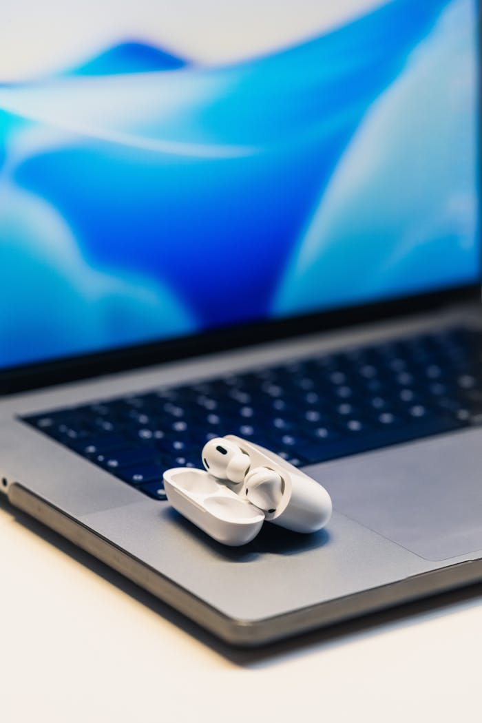 about-02 White wireless earbuds resting on a laptop with a vibrant blue screen background.