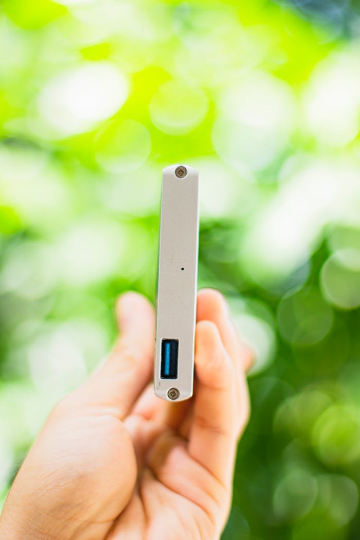 A hand holding a portable hard drive with a blurred green bokeh background.